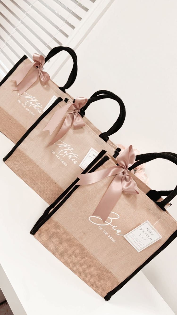 Three burlap tote bags with black handles, pink bows, and white calligraphy.