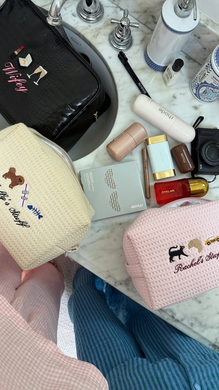 Embroidered cosmetic bags and makeup products arranged on a white marble bathroom counter.