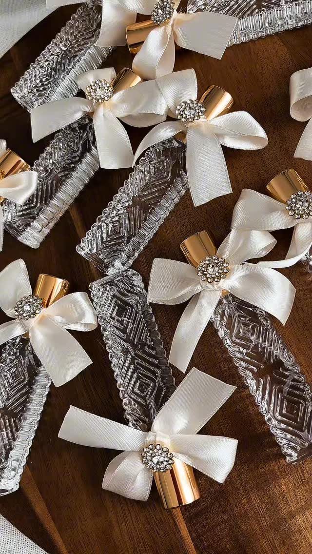 Textured glass bottles with white satin bows and rhinestones on a wooden table.