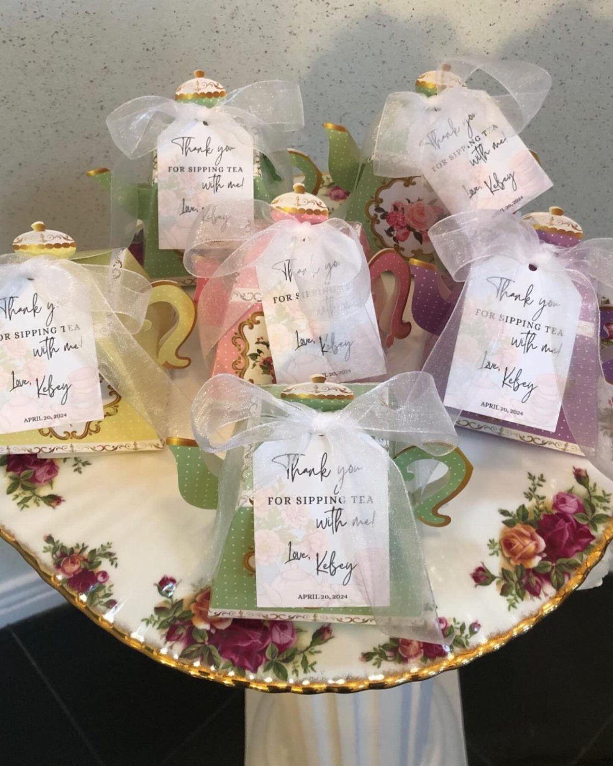 Colorful ceramic teapots wrapped in tulle with thank you tags on floral stand
