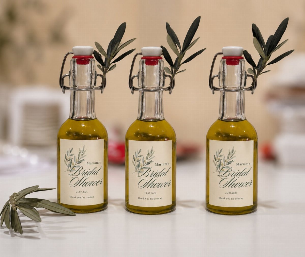 Three small olive oil bottles with bridal shower labels and fresh olive branches.