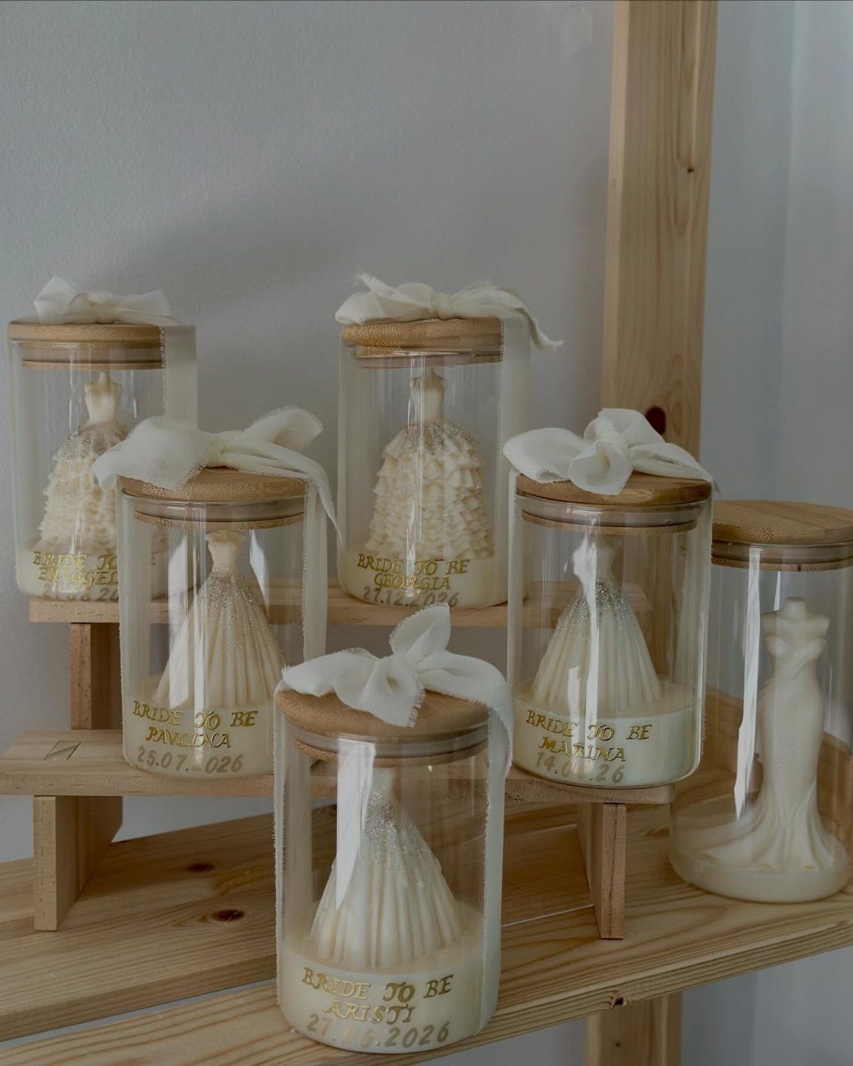 White wedding dress shaped candles in small glass jars with wooden lids and ribbons.