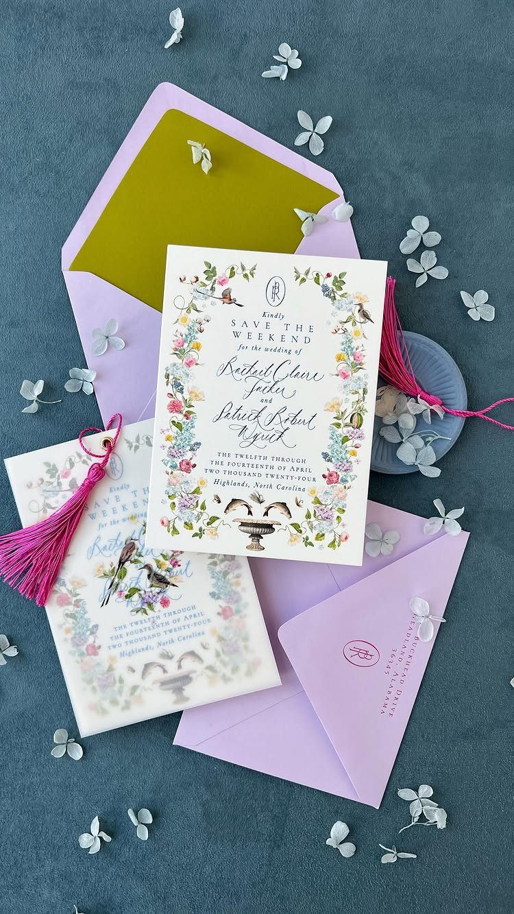 Colorful wedding invitations with floral designs and lavender envelopes on a grey background.