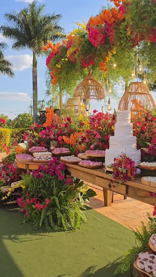 Outdoor wedding dessert table with a white cake and vibrant colorful floral arrangements.