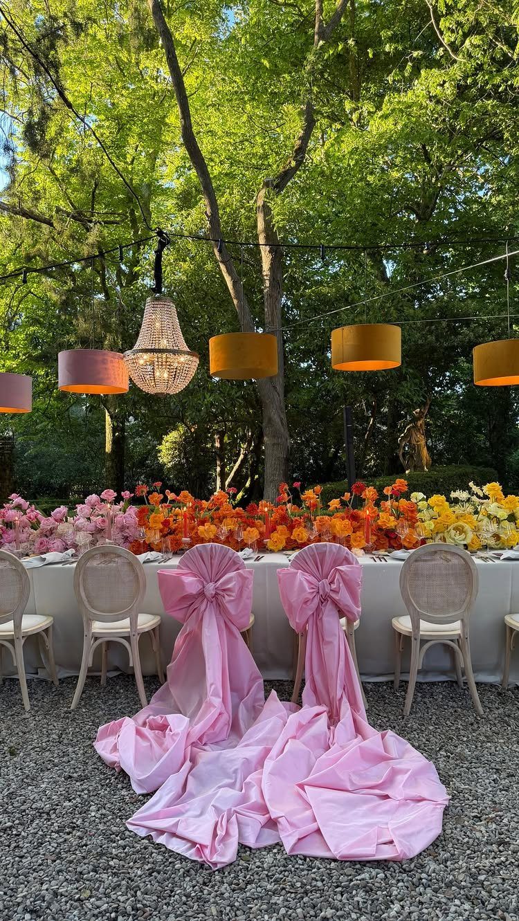 Wedding table with colorful floral runner and chairs draped in pink fabric bows.