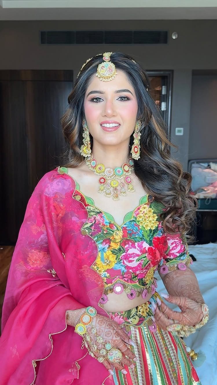 Woman in a colorful floral lehenga and traditional gold jewelry posing indoors.