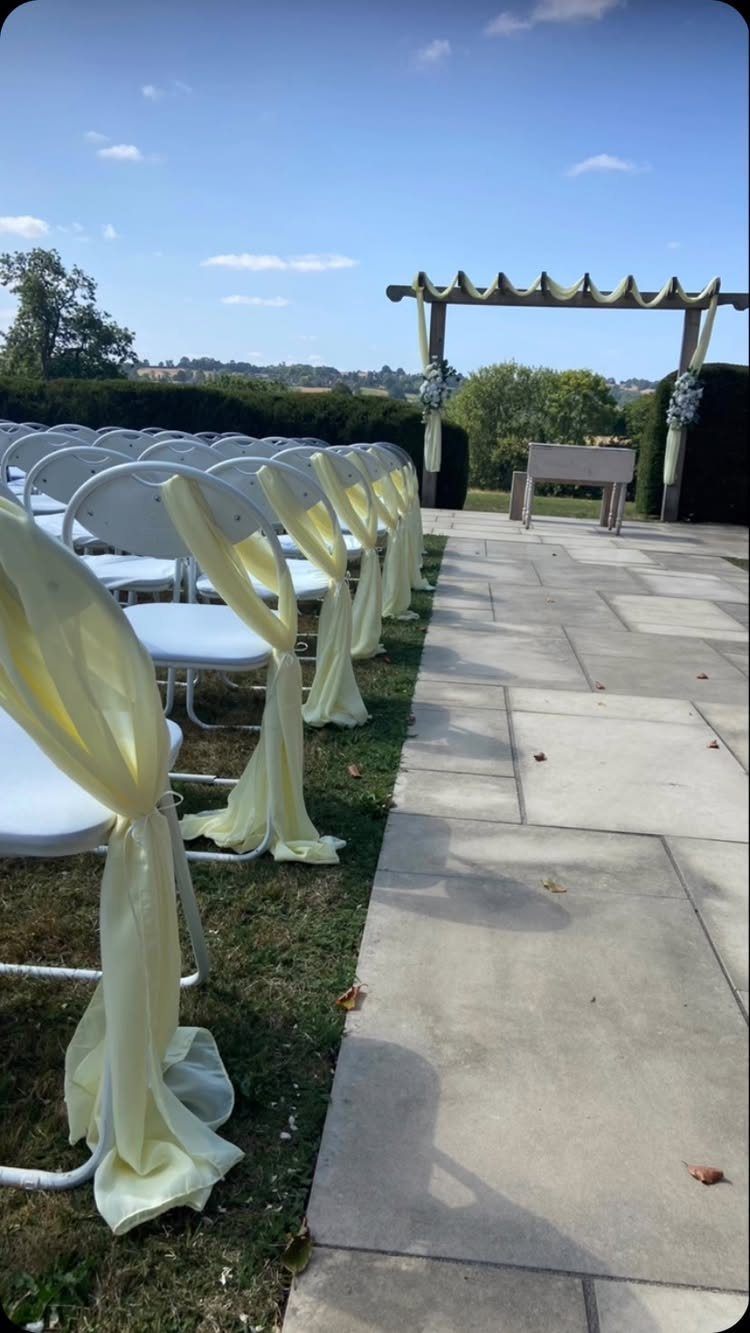 Wooden wedding arch draped in yellow fabric with matching yellow chair sashes outdoors