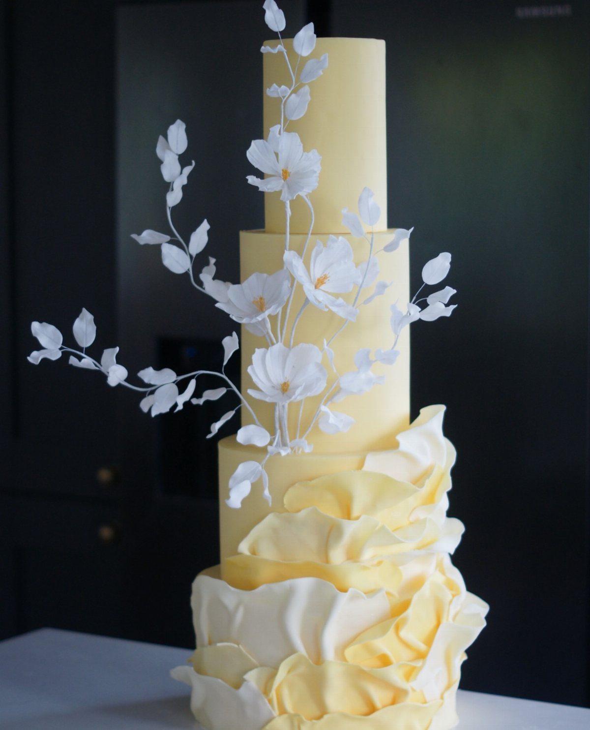Butter yellow tiered wedding cake with white sugar flowers and ruffled yellow petals.