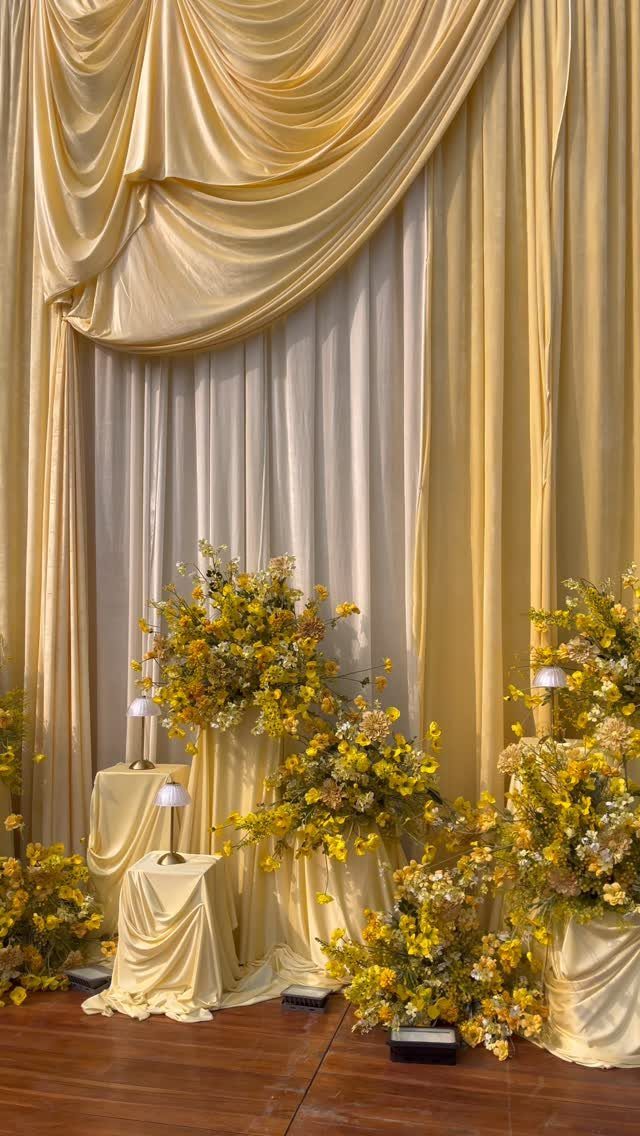 Butter yellow wedding backdrop with draped satin fabric and yellow floral arrangements.