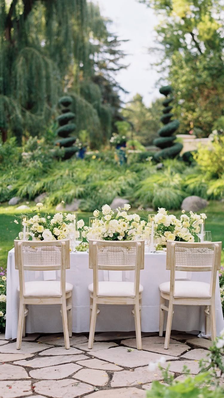 Pale yellow and white floral arrangements on a white wedding table in a garden