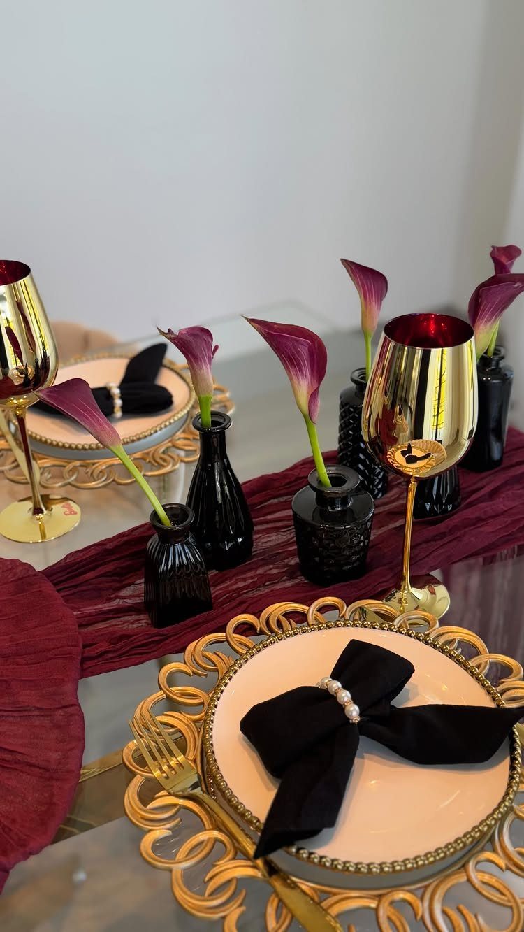 Burgundy calla lilies in small black vases on a decorated wedding table setting.