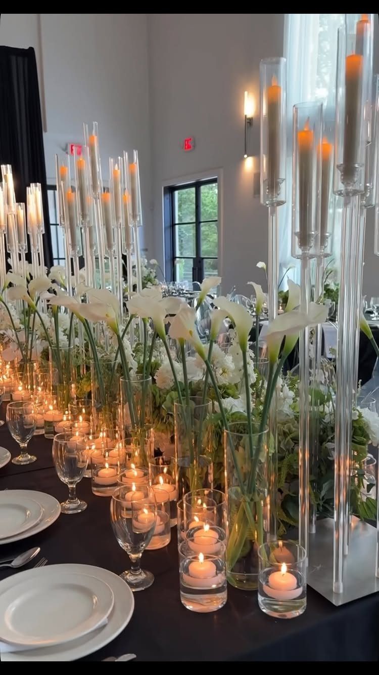 White calla lilies in glass vases surrounded by glowing floating tea light candles.