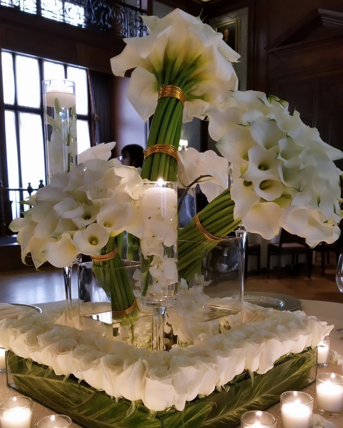 White calla lilies and roses centerpiece with candles on a wedding table.