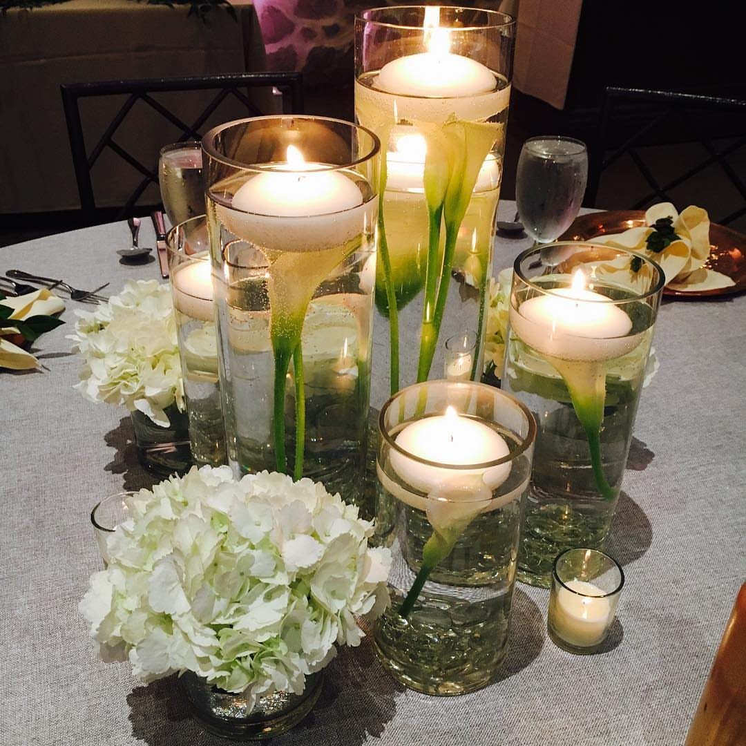 Floating white candles and calla lilies in glass cylinder vases on a wedding table