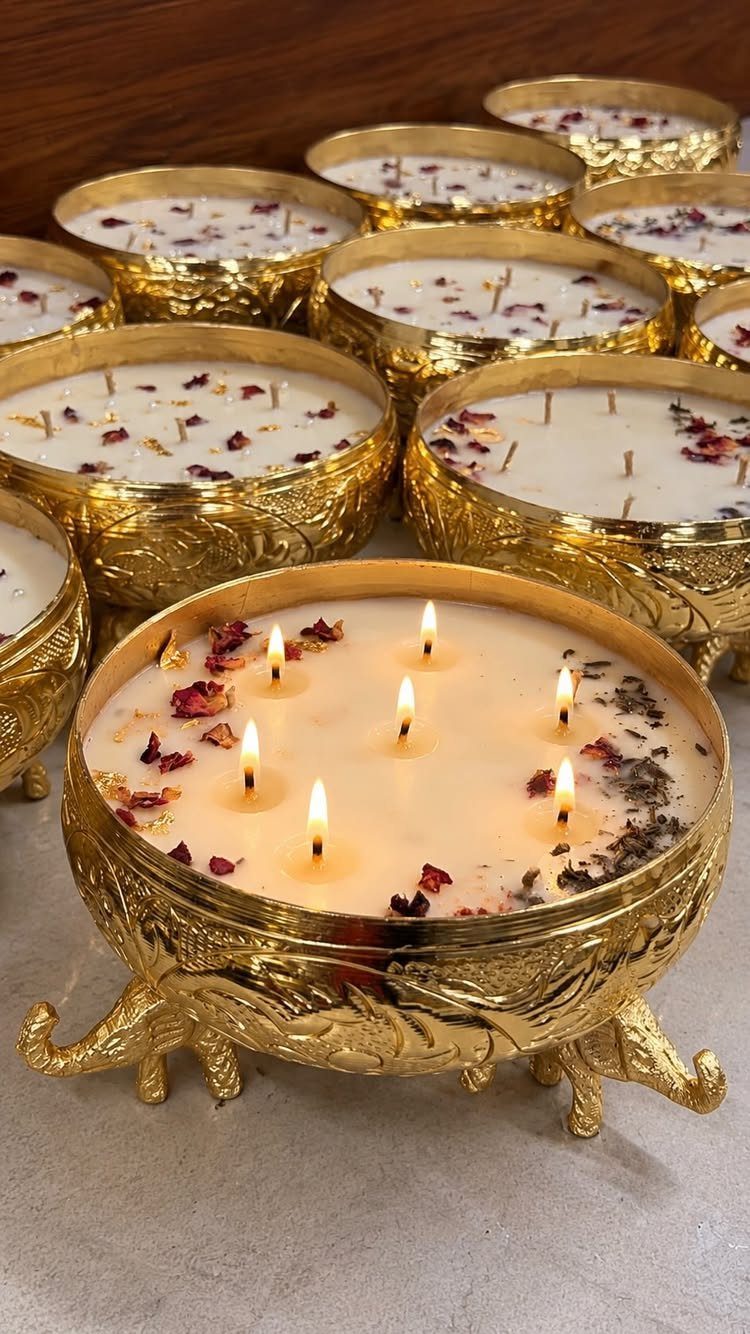 Six lit wicks in an ornate gold candle bowl with dried flower petals.