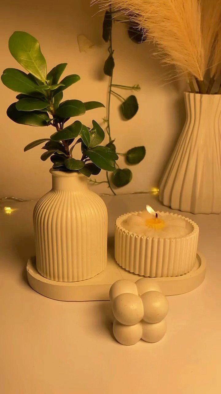 Lit white candle in a ribbed vessel next to a matching white vase.