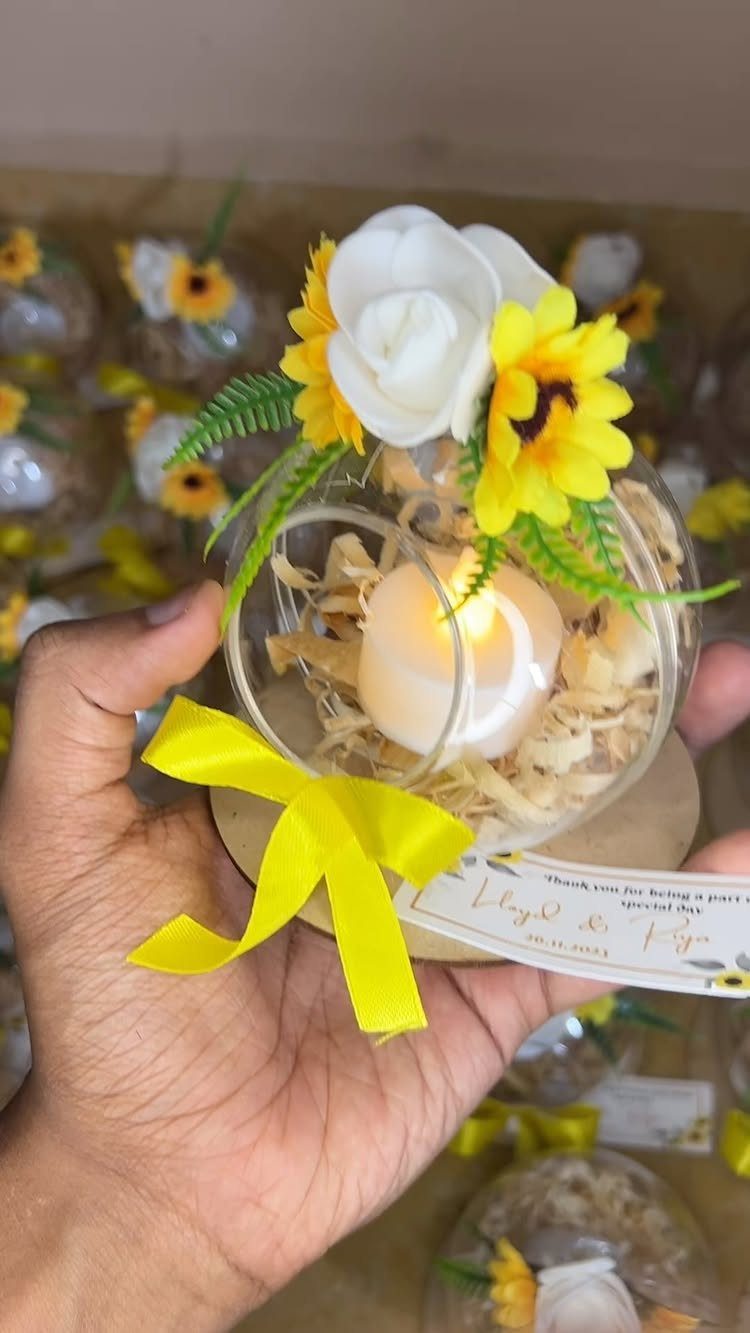 Lit tea light candle in a decorated glass globe with yellow flowers and ribbon.