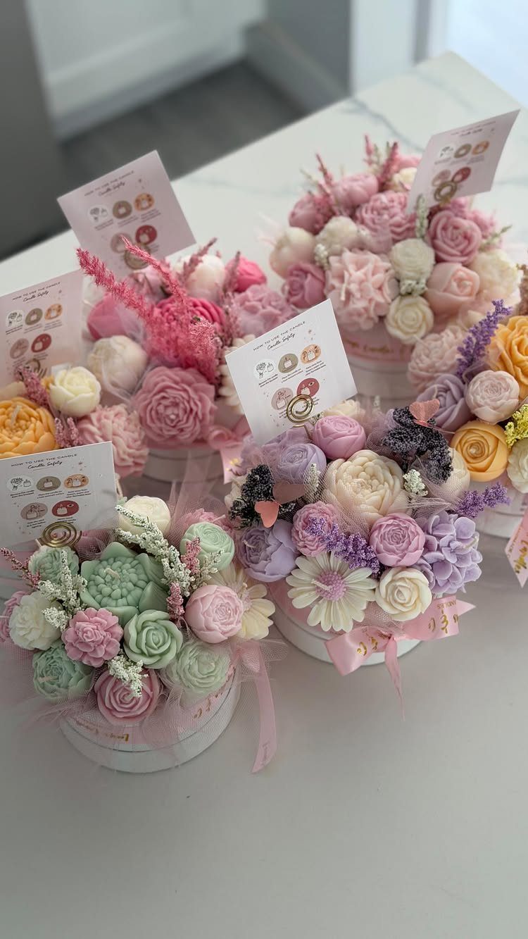 Pastel floral candles in white gift boxes with small attached tags.