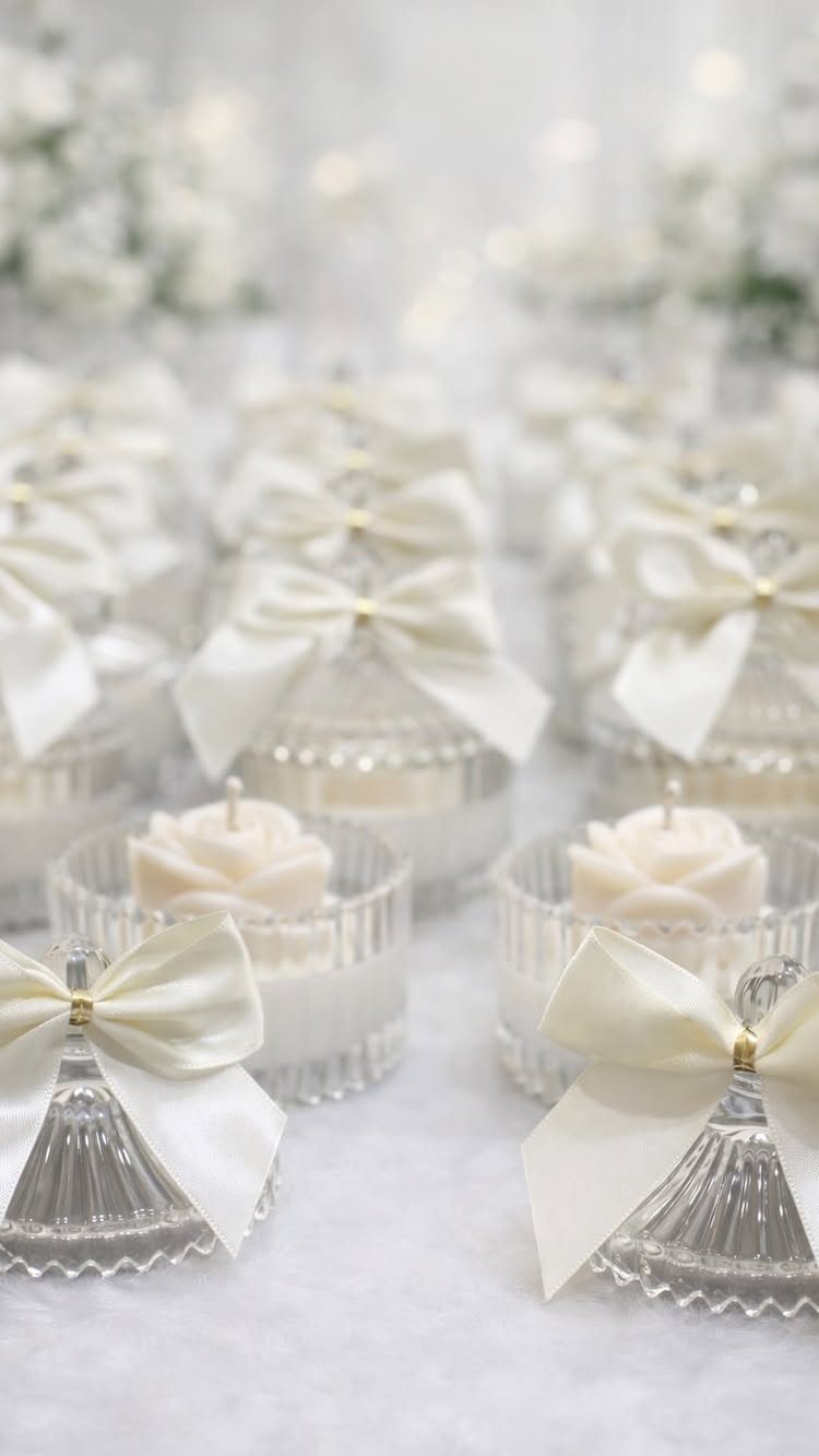 White rose-shaped candles in glass jars with satin bows for wedding gifts