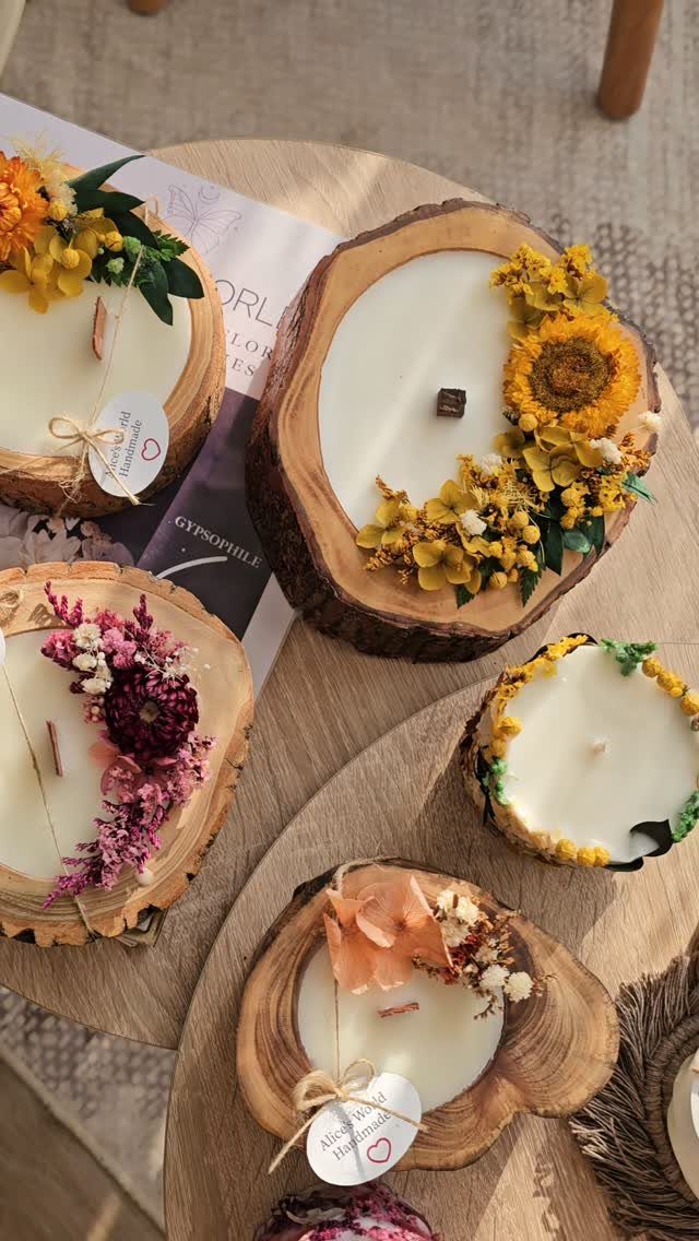 White candles in natural wood slice holders decorated with colorful dried flowers.