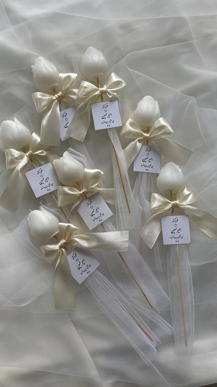 White tulip-shaped candles with cream satin bows and gift tags on white tulle.