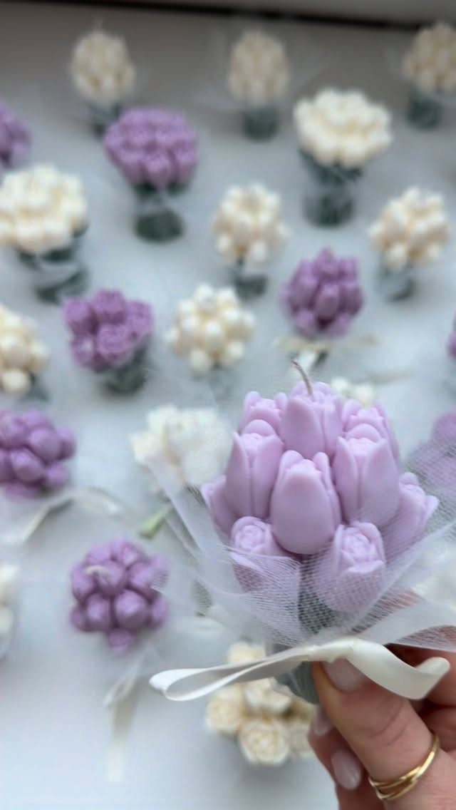 Purple tulip-shaped candle bouquet wrapped in white tulle and ribbon held by hand.