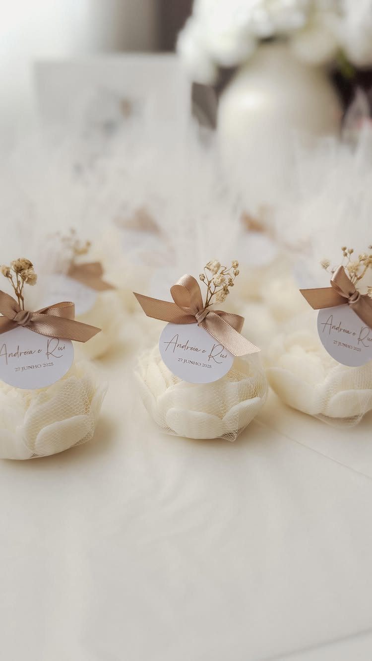 Rose-shaped white candles wrapped in tulle with gold ribbons and personalized tags.