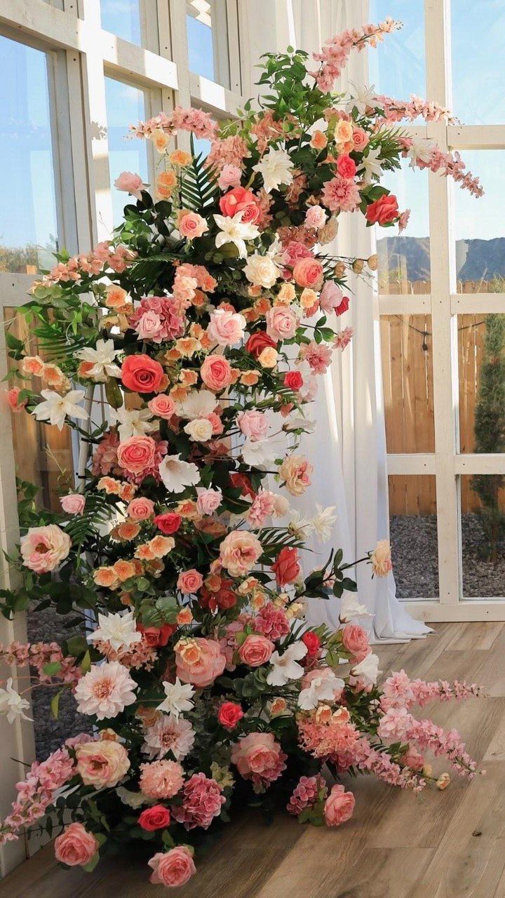 Asymmetrical floral arch with pink and white artificial flowers against a white window.