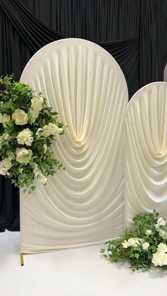Cream draped fabric wedding backdrops decorated with white roses and green foliage.
