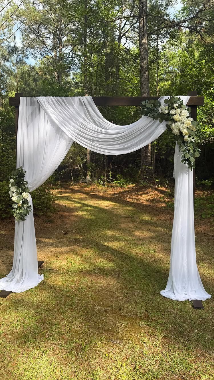 Wooden wedding arch draped in white fabric with white floral arrangements and greenery.