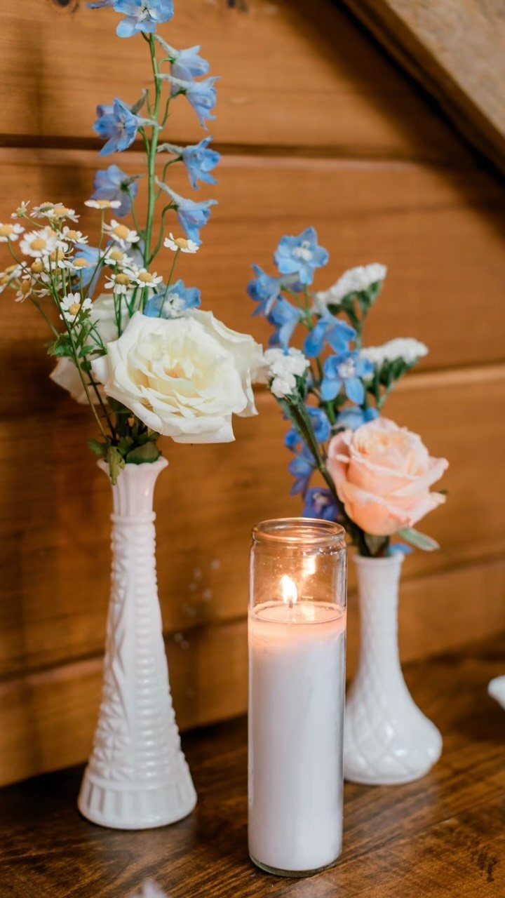 White ceramic vases with blue and peach flowers and a lit pillar candle.