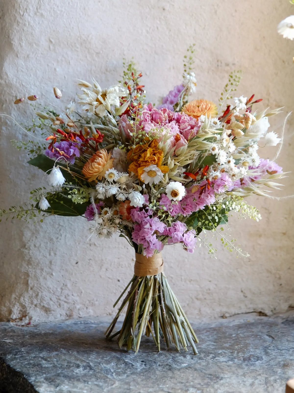 Dried flower bouquet with pink and orange blooms tied with twine on stone.
