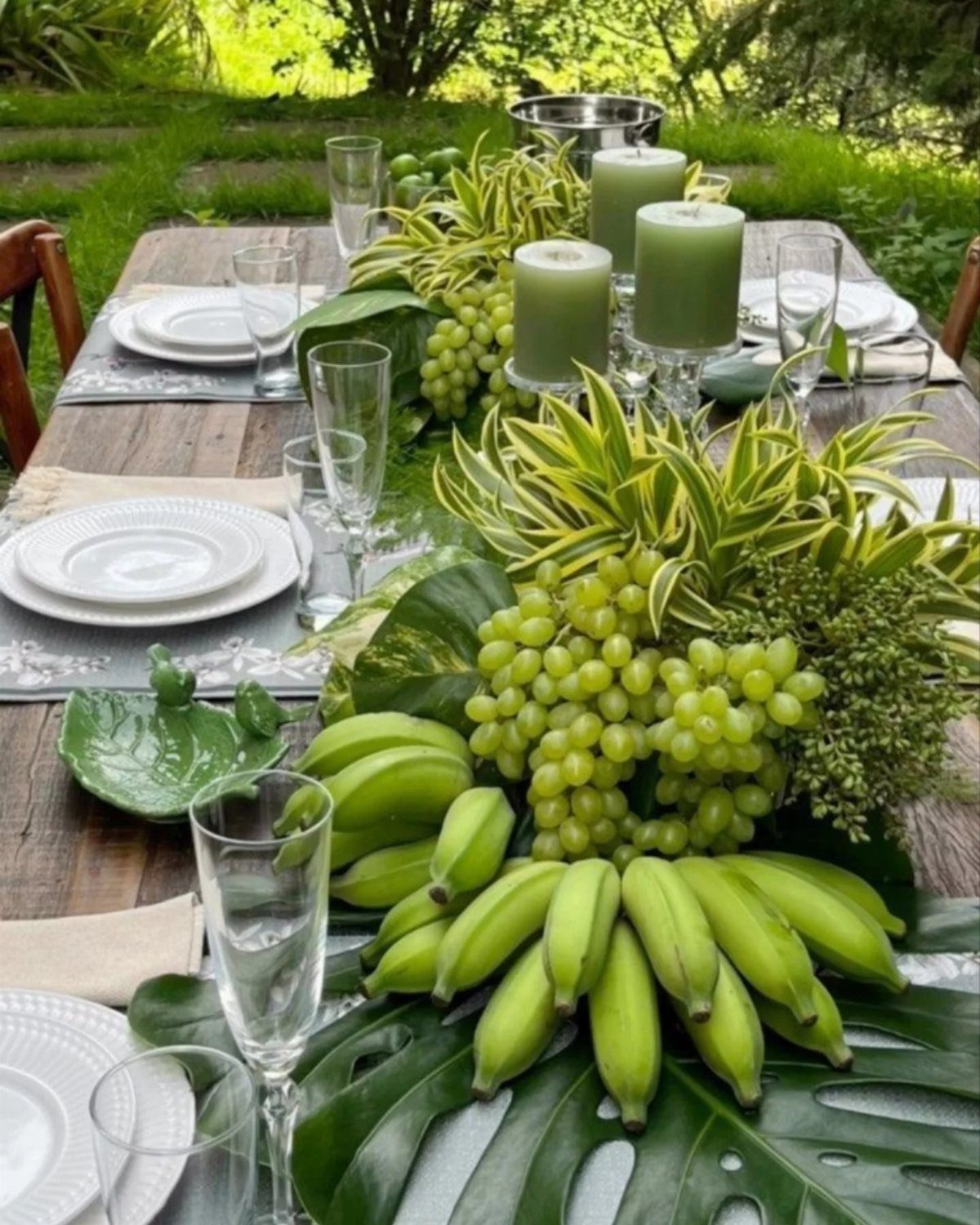 Green fruit centerpiece with bananas and grapes on a wooden outdoor table.