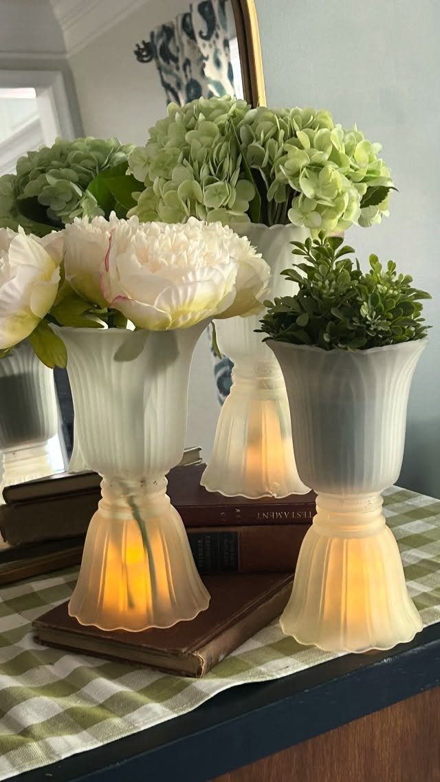 Frosted white glass vases with flowers and internal lighting resting on vintage books.