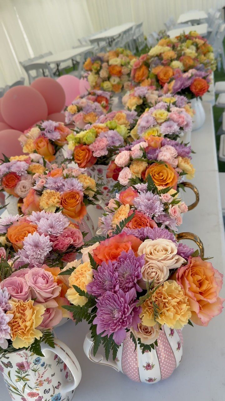 Colorful floral arrangements in patterned white teapots on a white table.