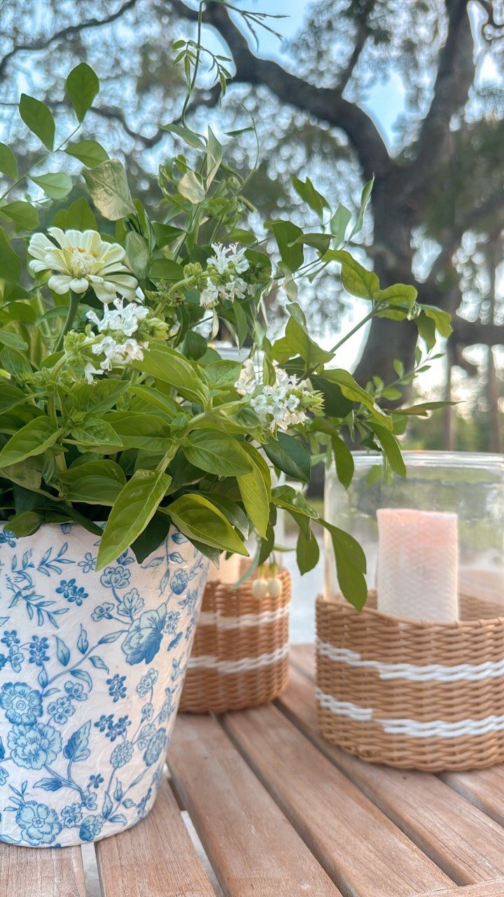 Blue floral vase with white flowers and wicker candle holders on wooden table