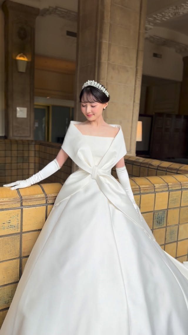 Woman in a classic white satin wedding gown with gloves and a tiara.