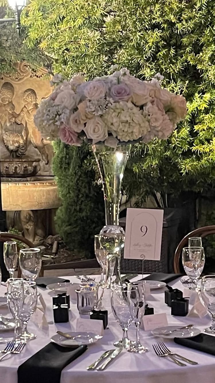 Floral centerpiece with roses and hydrangeas in a tall vase on a wedding table.