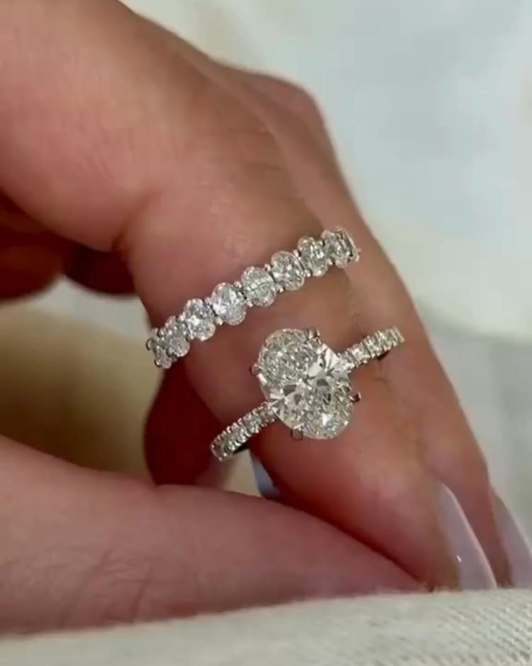 Two diamond wedding rings, one oval-cut and one eternity band, on a finger.