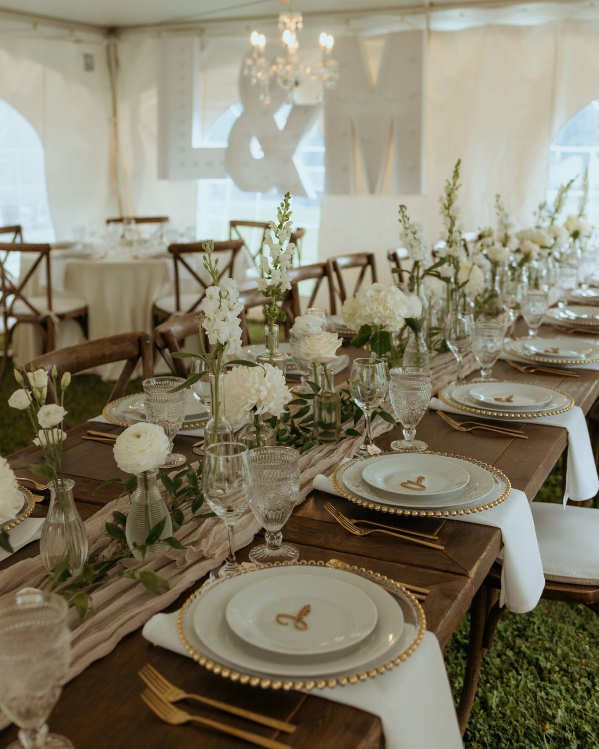 Wooden wedding table with white flowers and gold place settings under a white tent