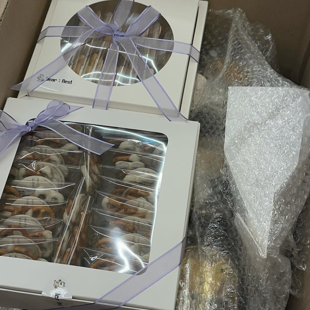 Chocolate covered pretzels in white gift boxes tied with purple ribbons in shipping box