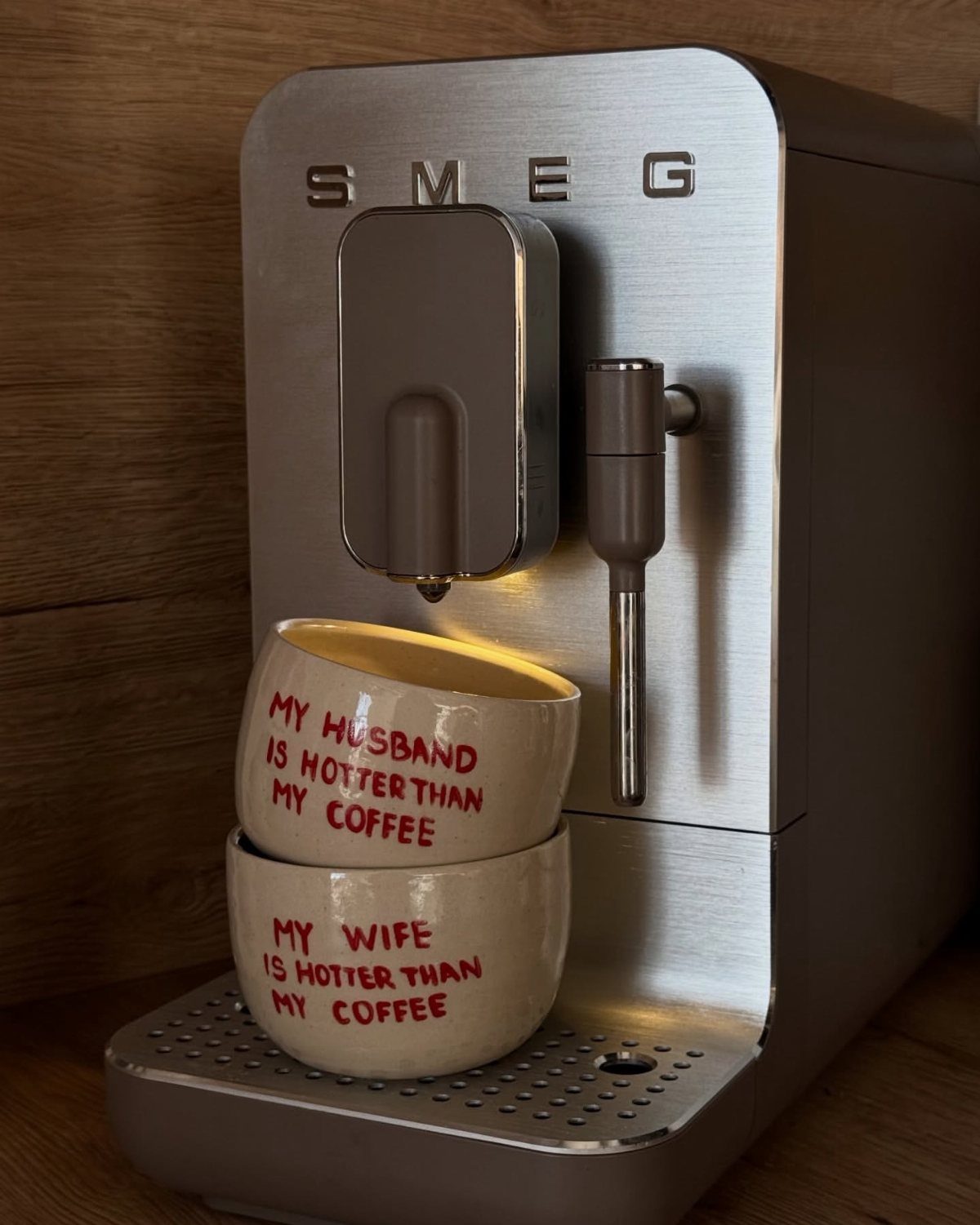 Two white ceramic mugs with romantic text stacked before a silver espresso machine.