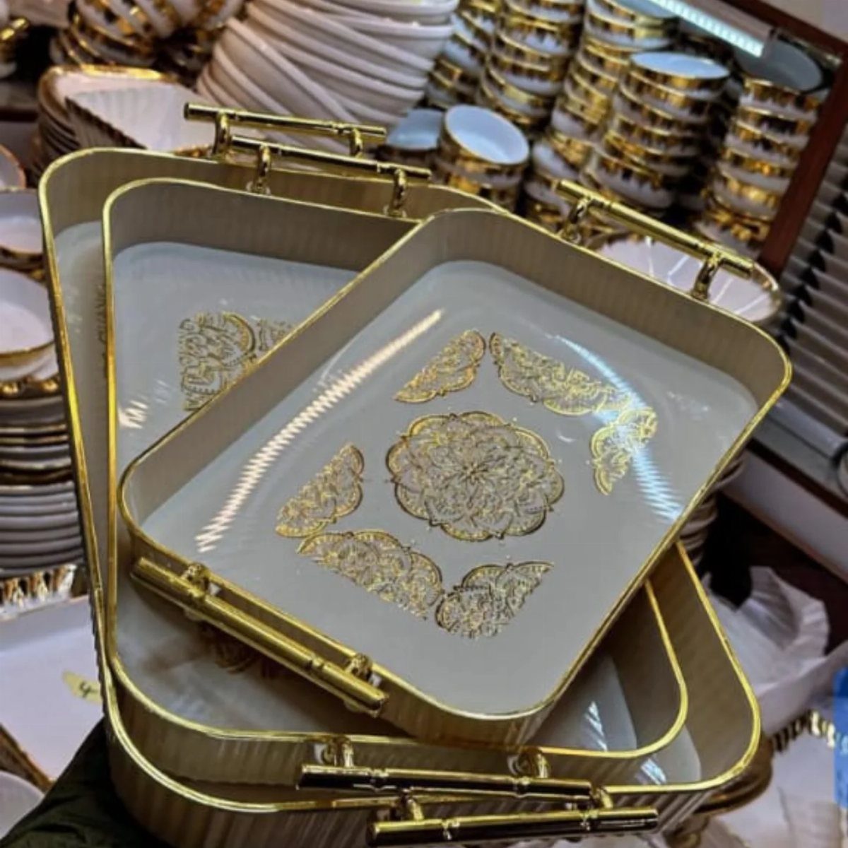 Gold and white serving trays with intricate floral patterns stacked in a store