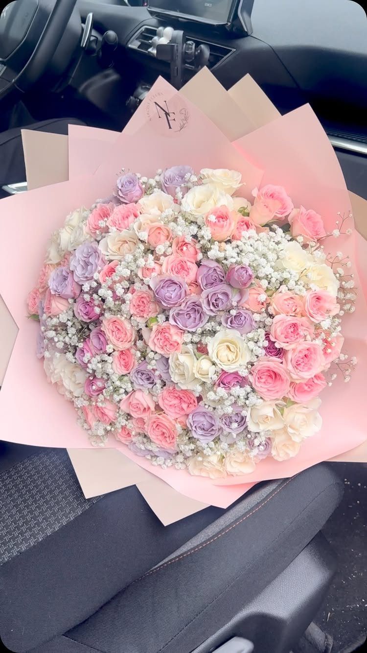 Large bouquet of pink, purple, and white roses wrapped in pink paper.
