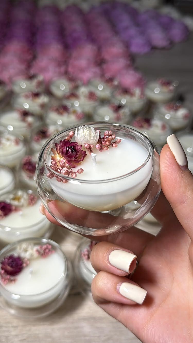 Hand holding a white scented candle in a glass bowl with dried flowers