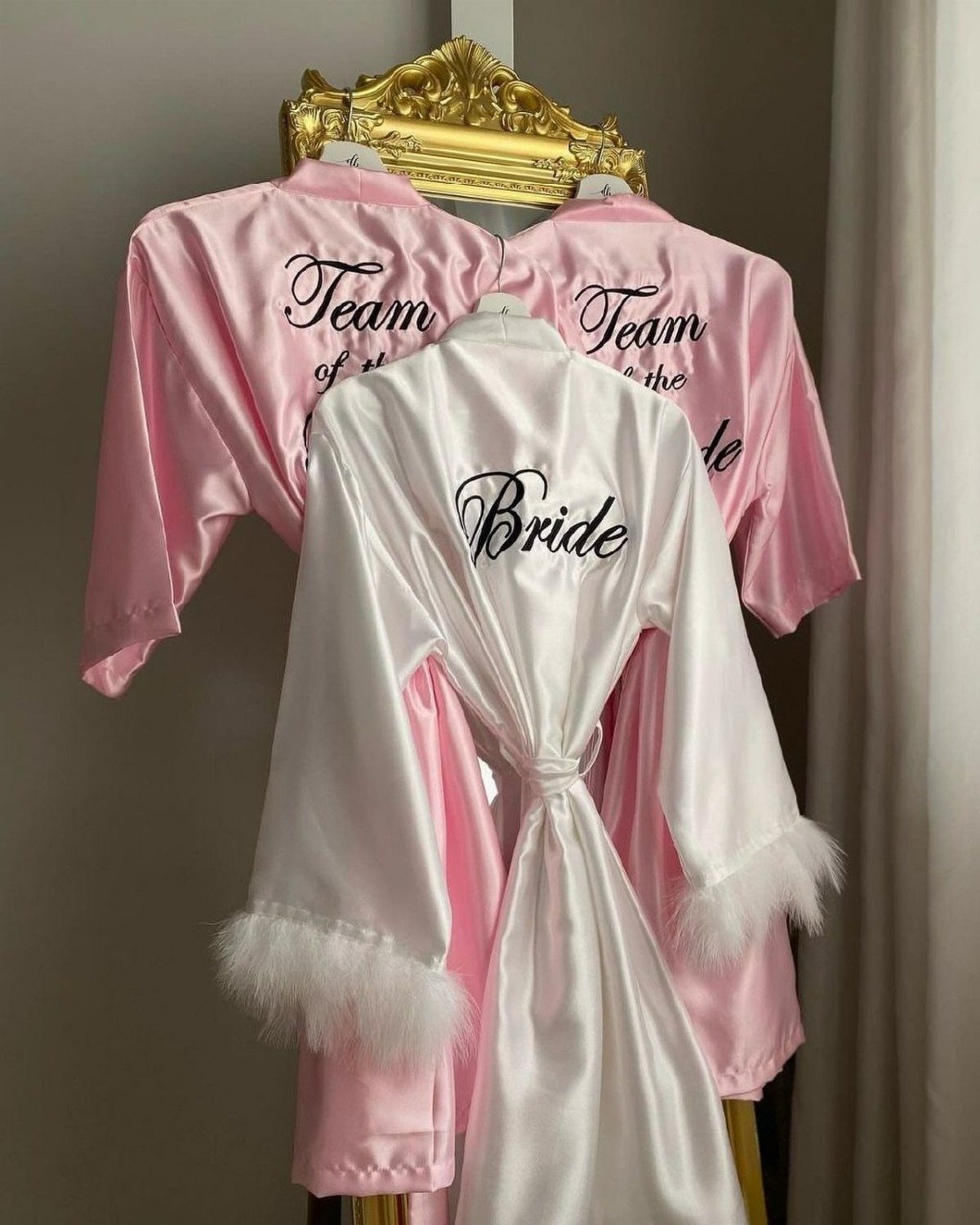 White bridal robe and pink bridesmaid robes hanging together with script lettering.
