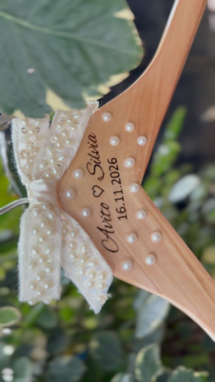 Wooden wedding dress hanger with engraved names, date, pearls, and a lace bow.