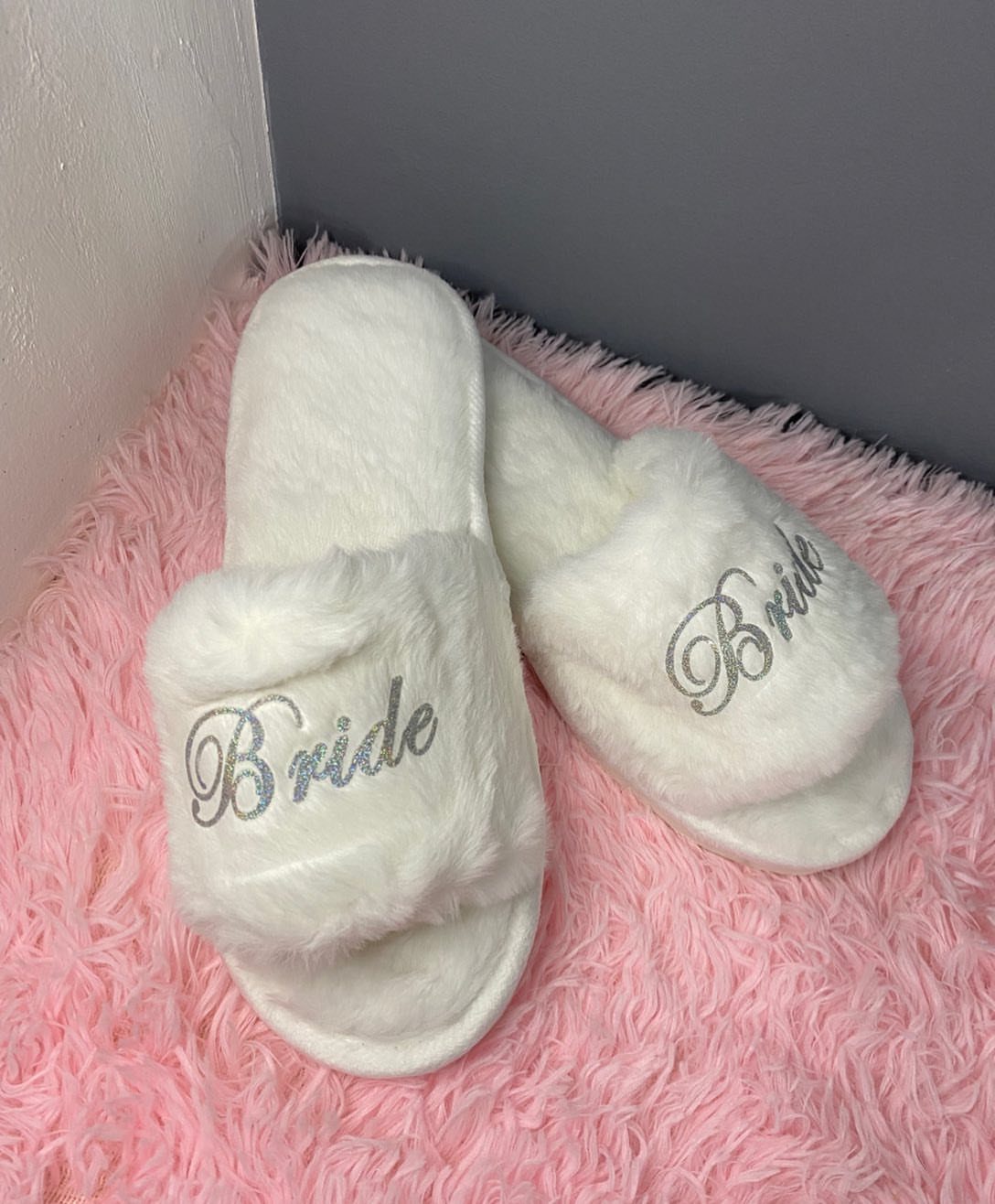 White fluffy bride slippers with silver glitter text on a pink shaggy rug