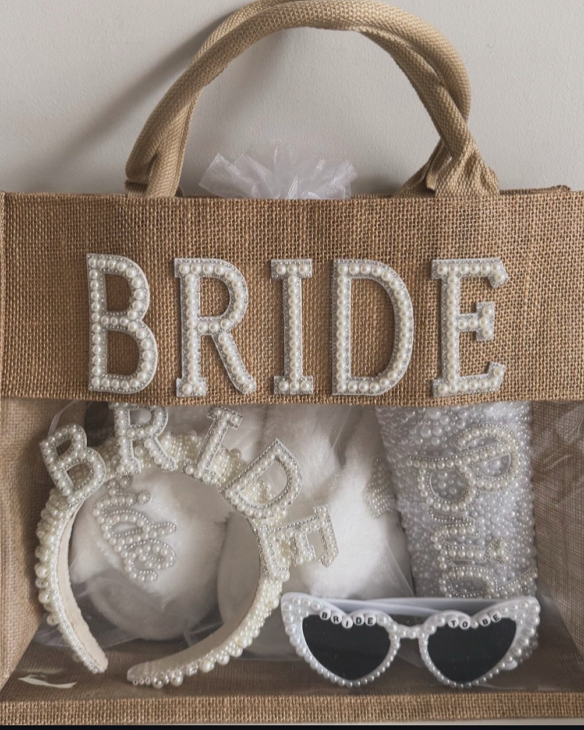 Burlap bride tote bag containing a pearl headband and heart-shaped sunglasses
