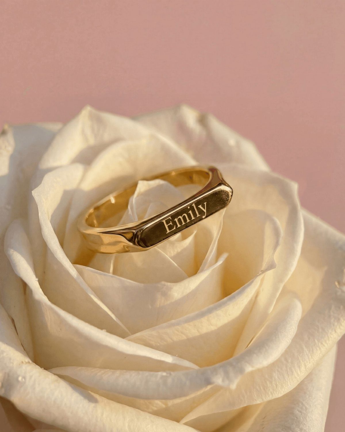 Gold ring engraved with Emily resting inside a white rose petal